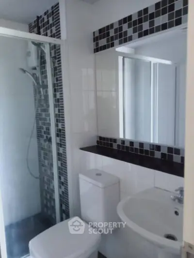 Modern bathroom with sleek black and white tile design and glass shower enclosure.