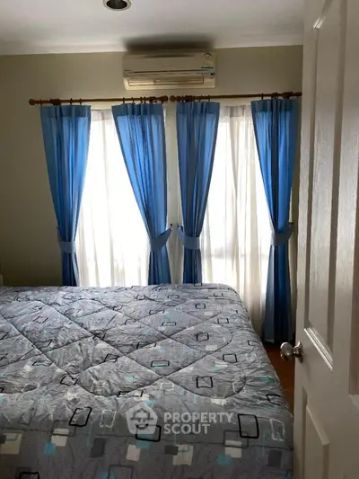 Cozy bedroom with natural light filtering through blue curtains, complete with air conditioning for comfort.