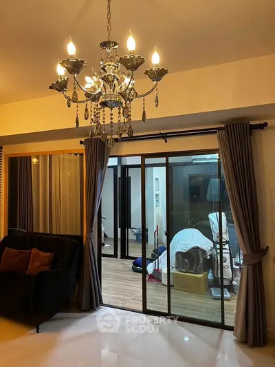 Elegant living room with chandelier and sliding glass doors leading to a cozy balcony.