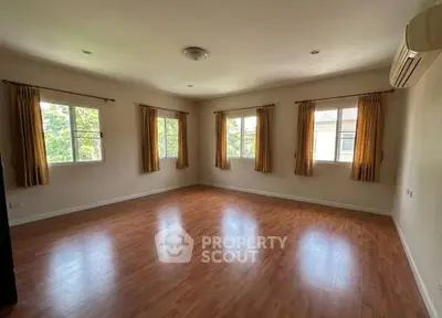 Spacious empty room with wooden flooring and large windows offering natural light.
