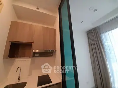 Modern kitchenette with sleek wooden cabinetry and stainless steel appliances, adjacent to a bright living area with floor-to-ceiling windows and elegant drapery.