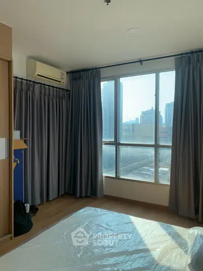 Spacious bedroom with large windows offering city views, featuring hardwood floors and air conditioning.