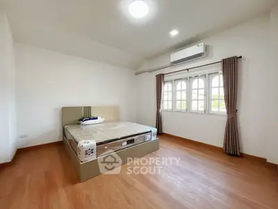 Spacious bedroom with wooden flooring and large window, featuring a comfortable bed and air conditioning.