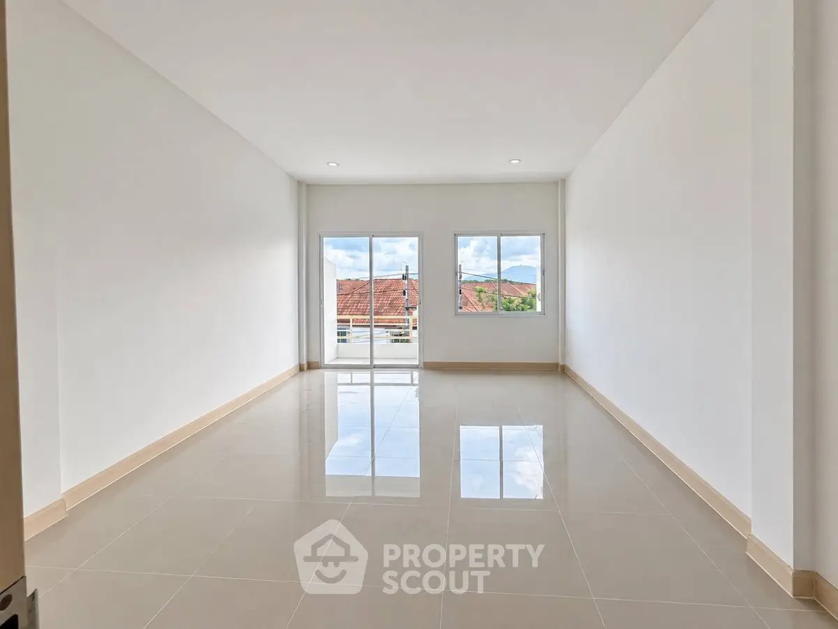 Spacious empty room with glossy tiled floor and large windows offering natural light and views.