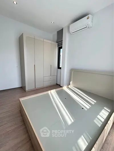 Modern bedroom with sleek wardrobe and air conditioning unit, featuring minimalist design and ample natural light.