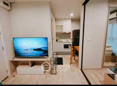 Modern open-plan living room with kitchen, featuring sleek furniture and a large TV.