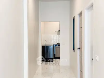 Modern hallway leading to a sleek kitchen with stainless steel appliances and elegant tile flooring.