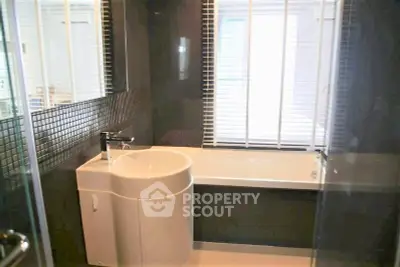 Modern bathroom with sleek design and bathtub, featuring large window with blinds.
