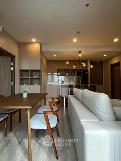 Modern open-plan living room with stylish kitchen and dining area, featuring elegant furniture and warm lighting.