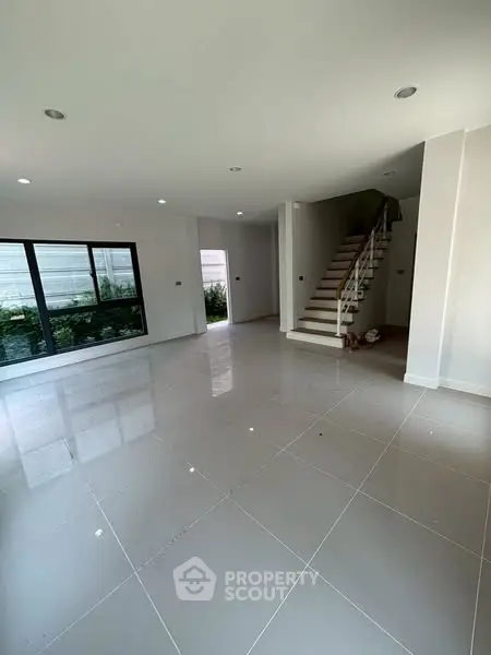 Spacious modern living room with glossy tiled floors and staircase, perfect for family gatherings.