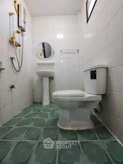 Compact bathroom with green tiled floor and white fixtures, featuring a round mirror and shower area.