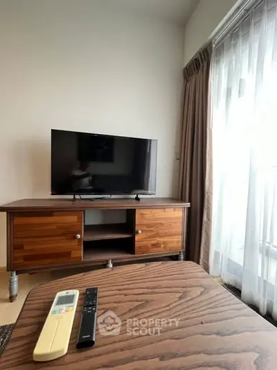 Cozy living room with wooden TV stand and large window for natural light.