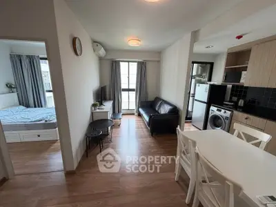 Modern apartment interior with open living room and kitchen, featuring wooden flooring and natural light.