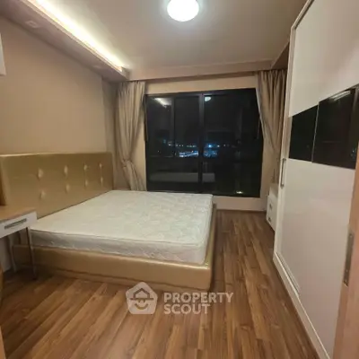 Spacious bedroom with modern design and large window offering city view, featuring wooden flooring and stylish furnishings.