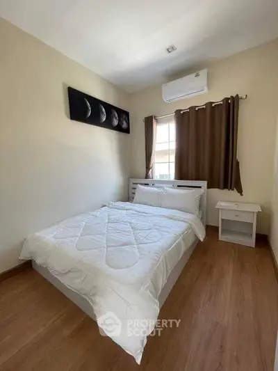 Cozy bedroom with wooden flooring and moon phase artwork, featuring a comfortable bed and air conditioning.