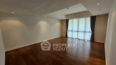 Spacious empty living room with wooden flooring and large window.