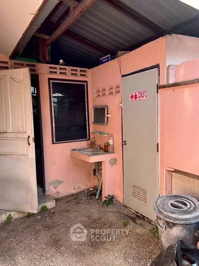 Outdoor restroom area with sink and pink walls, featuring a simple design.