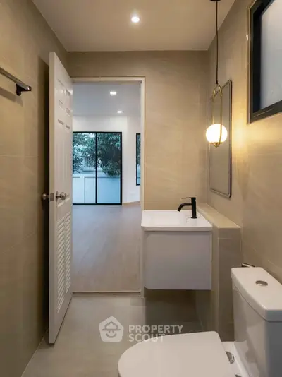 Modern bathroom with sleek fixtures and view into spacious room with large windows.