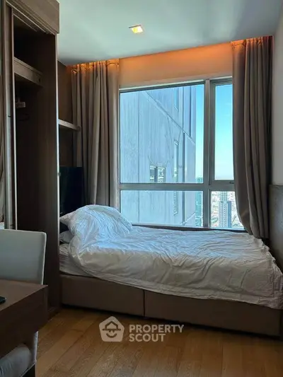 Cozy bedroom with large window offering stunning city views, perfect for urban living.
