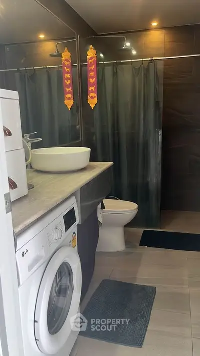 Modern bathroom with sleek design featuring a washing machine, vessel sink, and a full-sized shower with a dark curtain, offering functionality and style.