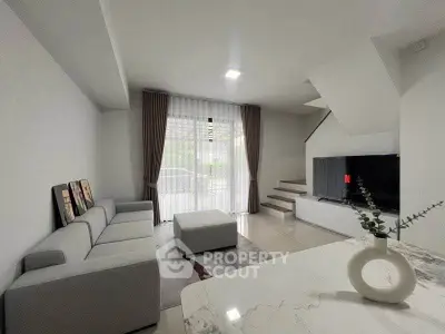 Modern living room with sleek gray sofa, stylish decor, and natural light from large window.
