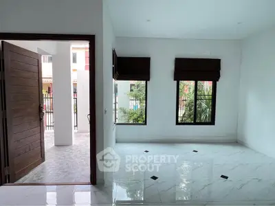 Spacious modern living room with large windows and marble flooring, opening to a charming outdoor patio.