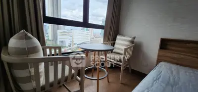 Cozy bedroom with city view, featuring stylish chairs and a small round table by the window.