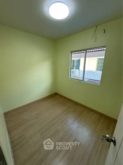 Bright empty room with wooden flooring and large window, perfect for customization.