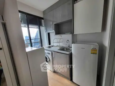 Modern compact kitchen with appliances and city view, featuring washing machine and fridge.
