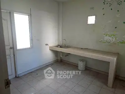 Spacious kitchen with minimalist design and ample natural light, featuring a long countertop and tiled flooring.