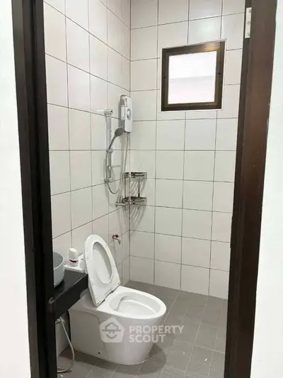 Modern bathroom with white tiles and compact design, featuring a toilet and shower area.