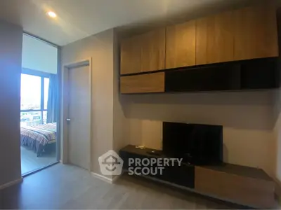 Modern living room with sleek wooden cabinetry and TV, adjacent to a cozy bedroom with city view.