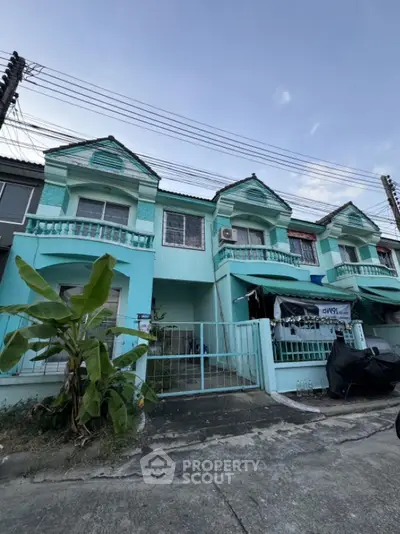 Charming turquoise townhouse with balcony and gated entrance in a serene neighborhood.