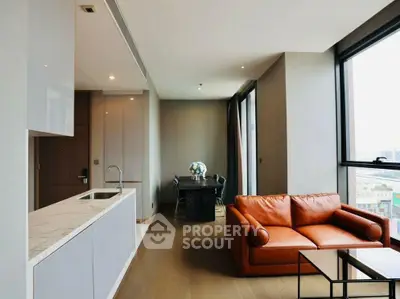 Modern living room with open kitchen and city view, featuring a stylish leather sofa and elegant dining area.
