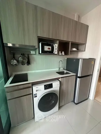 Modern compact kitchen with washing machine, microwave, and fridge in sleek cabinetry.