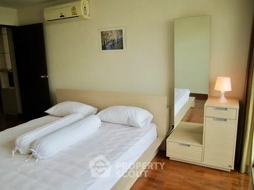 Spacious bedroom with modern decor and ample natural light, featuring a large mirror and cozy ambiance.