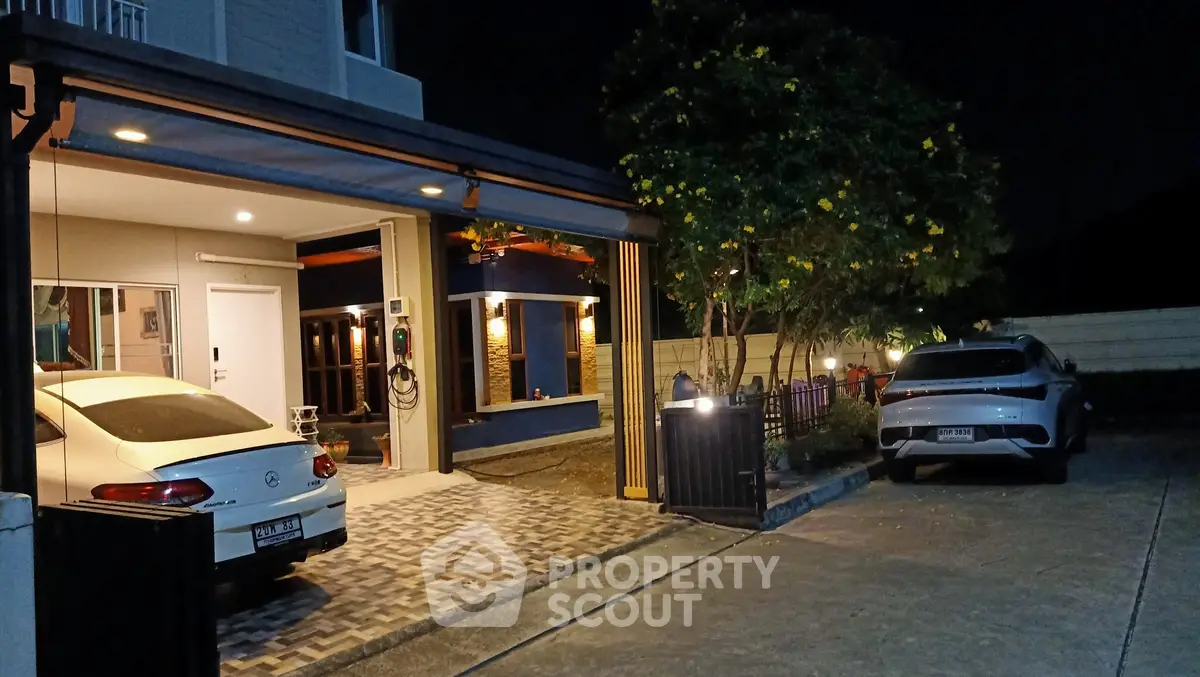 Modern home exterior with spacious driveway and parked cars at night