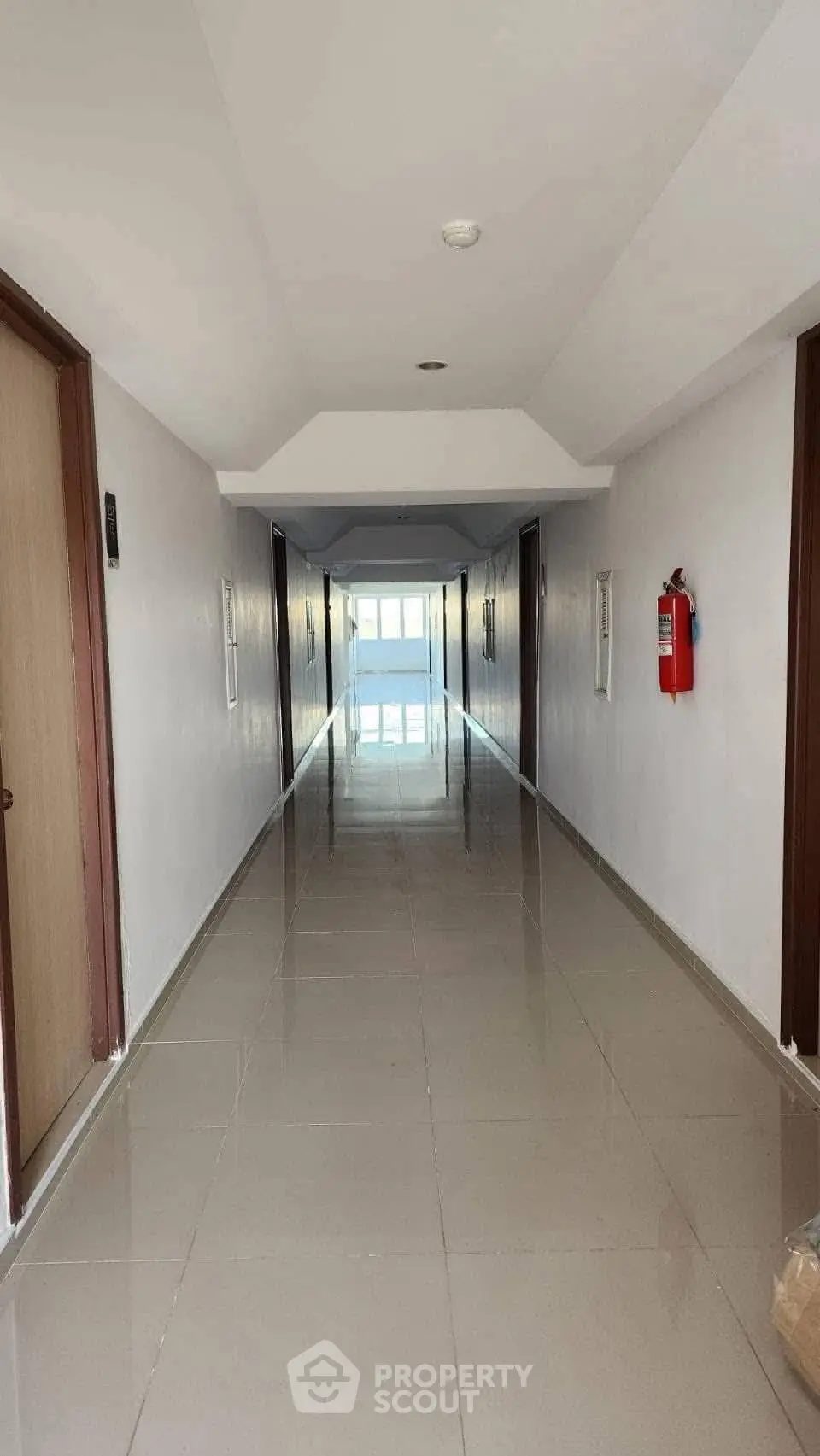 Modern apartment building corridor with polished tile flooring and fire safety equipment.
