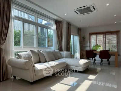 Spacious living room with elegant sofa and dining area, featuring large windows and natural light.