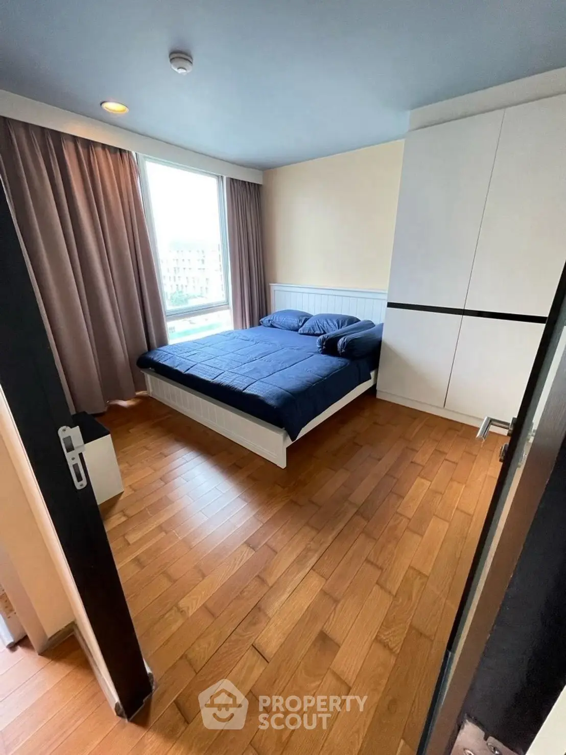 Cozy bedroom with wooden flooring and large window offering natural light.