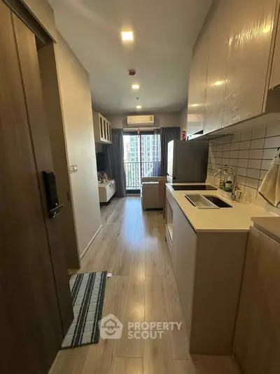 Modern apartment kitchen with sleek cabinetry and bright living area leading to a balcony with city views.