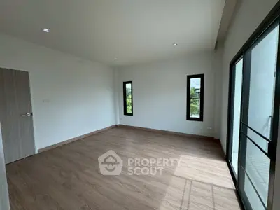 Spacious empty room with wooden flooring and large windows offering natural light.