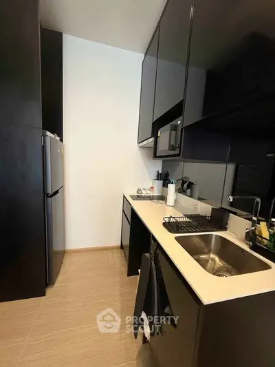 Modern kitchen with sleek black cabinets and stainless steel appliances in a compact layout.