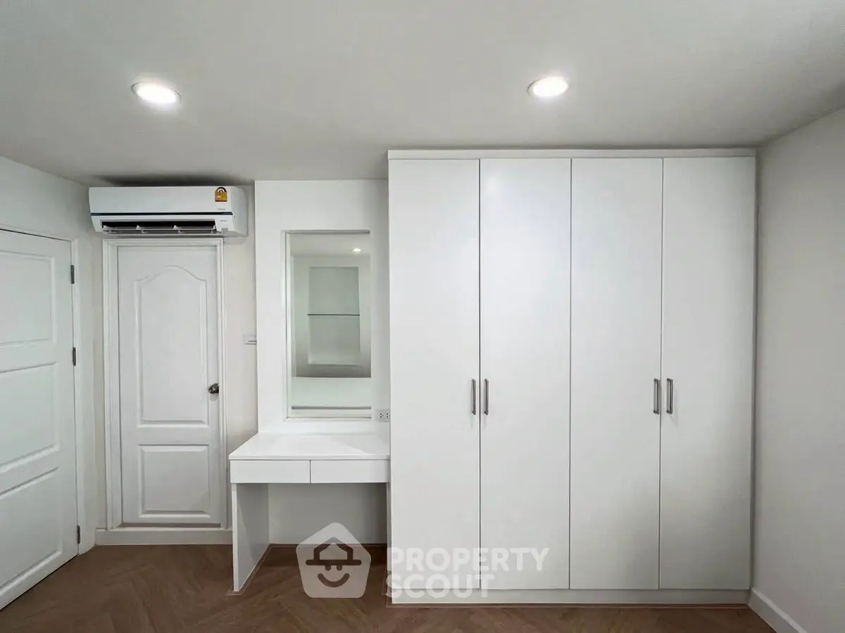 Modern bedroom with built-in wardrobe and vanity, featuring sleek white design and wooden flooring.