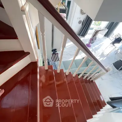 Elegant wooden staircase leading to a bright, modern living area with marble flooring and stylish decor.