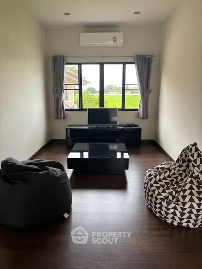 Cozy living room with bean bags and a view of lush greenery through large windows.