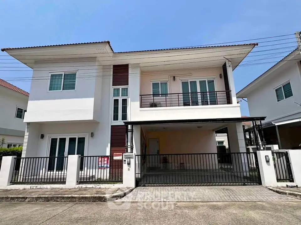 Modern two-story house with balcony and gated driveway in sunny neighborhood.