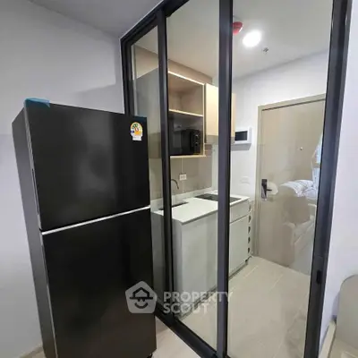 Modern kitchen with sleek black fridge and glass sliding doors in a compact apartment.