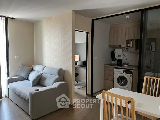 Modern apartment interior with an open layout connecting a cozy living room to a sleek kitchen featuring a washing machine and built-in oven.