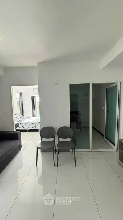 Spacious modern living room with sleek white tiles and glass sliding doors leading to a bright bedroom.